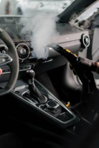 The concept of car cleaning and detailing The detailing master cleans the car interior with a hot steam cleaner Cleaning the car interior