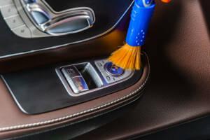 A man cleaning car interior panels and dashboard with yellow mic